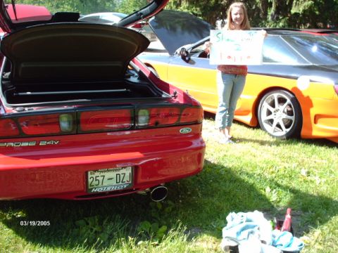 1995 Ford Probe - A red 1995 Ford Probe is parked next to an orange and black car, with a girl holding a sign.
