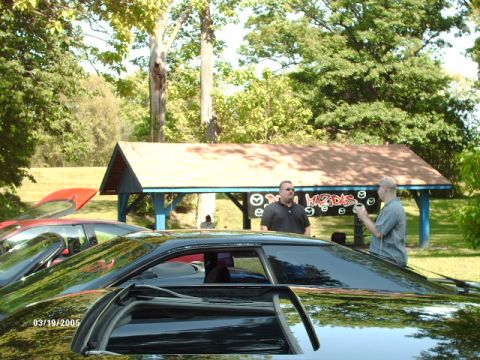 1995 Ford Probe - Two men stand near a pavilion with 'Mazdas' painted on it, with cars in the foreground.