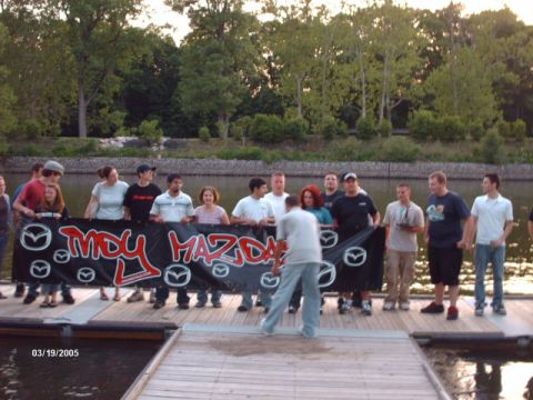 1995 Ford Probe - A group of people stand on a wooden dock holding a banner that reads "IMDY MAZDA" with Mazda logos.