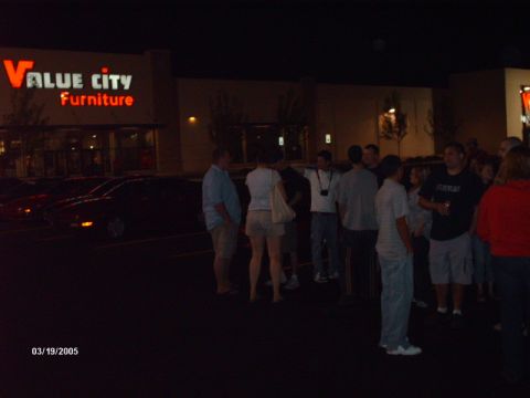 1995 Ford Probe - People stand in a parking lot in front of a Value City Furniture store after dark.