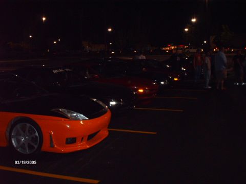 1995 Ford Probe - A line of cars are parked in a lot at night, with the front of a two-tone sports car in the foreground.