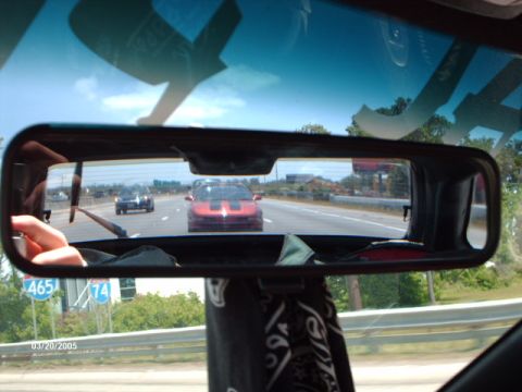 1995 Ford Probe - A red sports car is seen in the rearview mirror while driving on the highway, with other vehicles and road signs visible.