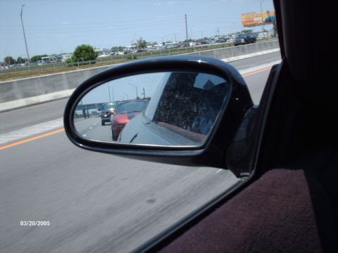 1995 Ford Probe - Traffic on the highway viewed through a side mirror, showing multiple vehicles including a red car.