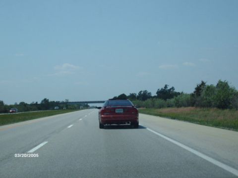 1995 Ford Probe - A red sports car cruises down the highway on a clear day, with a bridge visible in the distance.
