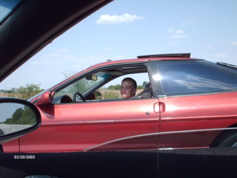 1995 Ford Probe - A red 1995 Ford Probe is seen from the side with a young male driver behind the wheel and the sunroof open.