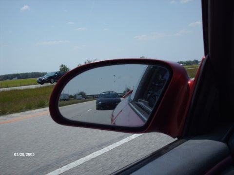 1995 Ford Probe - A view from a car's side mirror shows another vehicle on the highway under a clear sky.