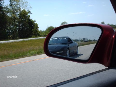 1995 Ford Probe - A black coupe is seen in the side mirror of a red car on a highway.