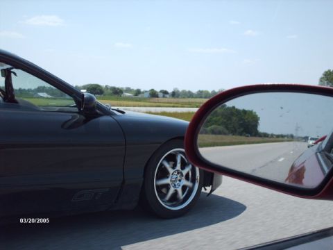 1995 Ford Probe - A black car with a GT badge is seen from the passenger side mirror while driving on a highway.