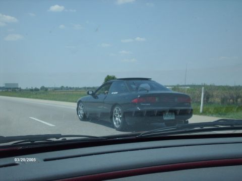 1995 Ford Probe - A black coupe is seen from the perspective of another vehicle on a highway under a partly cloudy sky.
