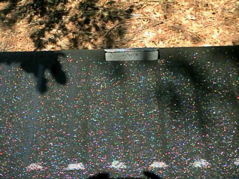 1976 Ford Ranchero - A close-up view of a vehicle part a sparkling black finish and a chrome accent strip.