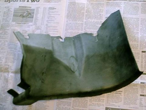 1976 Ford Ranchero - A fragment of a dark green automotive fender liner rests on a page of newspaper.