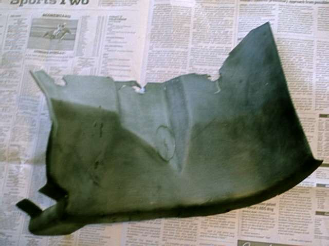 Dark green automotive fender liner fragment on newspaper