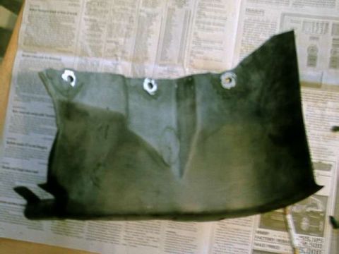 1976 Ford Ranchero - A black plastic automotive part with visible mounting holes rests on a surface covered with newspaper pages.