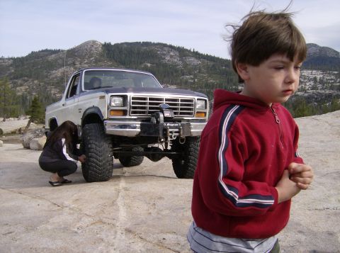 1986 Ford Bronco - A lifted 1986 Ford Bronco is parked outdoors while a person checks its tire.