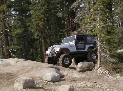 1986 Ford Bronco - A Jeep navigates a rocky off-road path surrounded by trees.