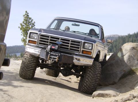 1986 Ford Bronco - A modified Ford Bronco navigates a rocky trail, with another vehicle partially visible on the left.