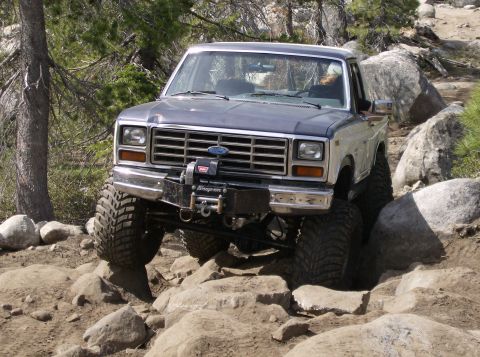 1986 Ford Bronco - Ford F-Series pickup truck with a winch is shown off-roading on a rocky trail.