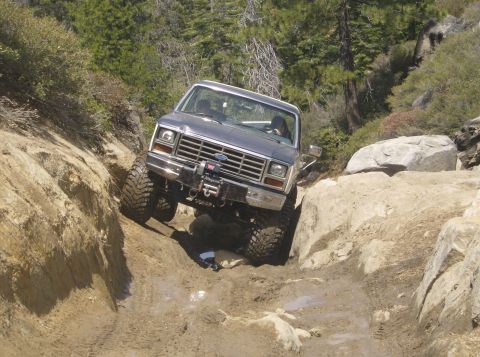 1986 Ford Bronco - This lifted Ford Bronco is tackling a challenging rocky trail with steep inclines and large boulders.