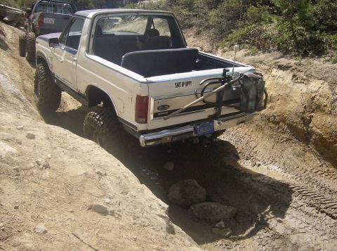 1986 Ford Bronco - White Ford Bronco navigates a challenging off-road trail with another vehicle behind it.
