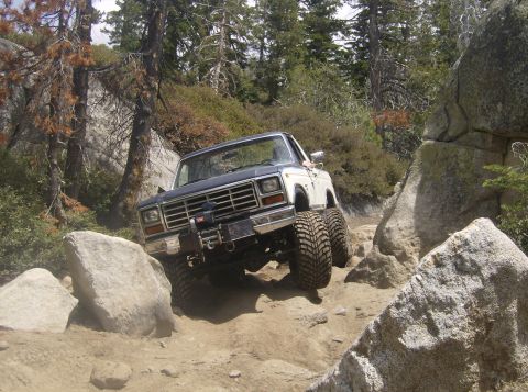 1986 Ford Bronco - Ford Bronco tackling a challenging off-road course with large boulders and trees.