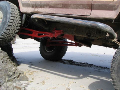 1983 Ford Bronco - The side profile of a 1983 Ford Bronco is visible, with its chassis and large tires positioned on a sandy terrain.