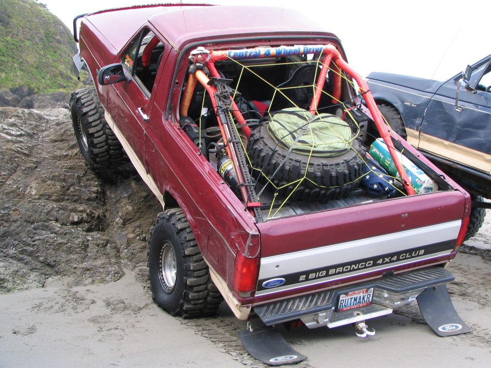 Topless maroon Ford Bronco with roll cage crawling rocks on a beach