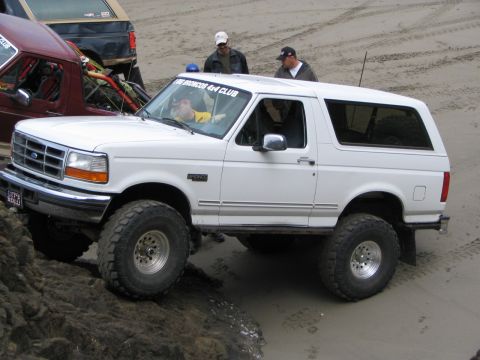 1983 Ford Bronco - White Ford Bronco with off-road tires navigates sandy terrain alongside other vehicles.