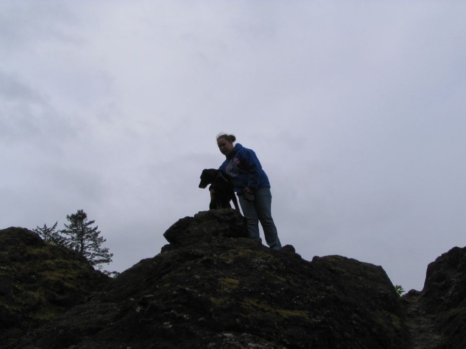 Person and dog standing on a rocky outcrop under an overcast sky