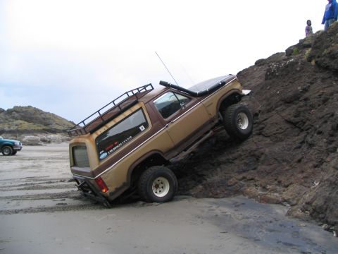 1983 Ford Bronco - Ford Bronco attempts to climb a rocky embankment next to a sandy beach, with another vehicle visible in the background.