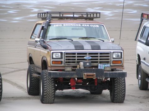 1983 Ford Bronco - A modified Ford Bronco with a snorkel and roof rack sits on a sandy beach next to another vehicle.