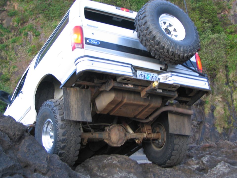 Underside rear view of a white lifted Ford Bronco flexed on rocks