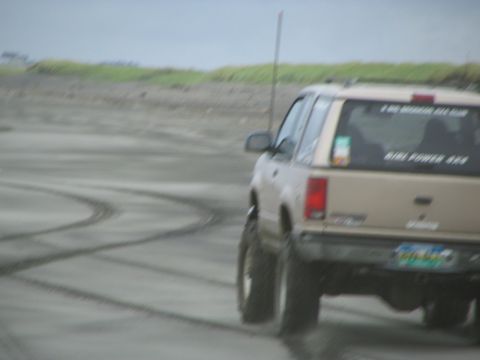 1983 Ford Bronco - Tan Ford Explorer with lifted suspension driving on a sandy surface, leaving tire tracks.