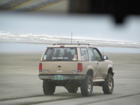 1983 Ford Bronco - This SUV is driving on the beach with the ocean waves in the background.
