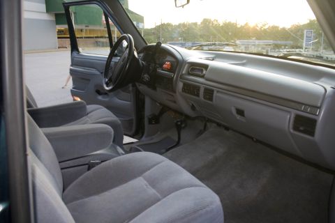 1995 Ford Bronco - Wide interior view of a 1990s Ford truck taken from the rear passenger area, showing gray cloth front bucket seats, the gray dash with glov…