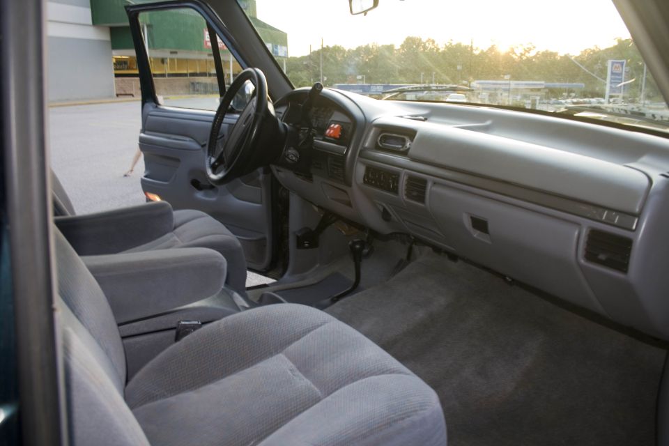 Gray cloth bucket seats and dashboard inside a 1990s Ford truck at sunset