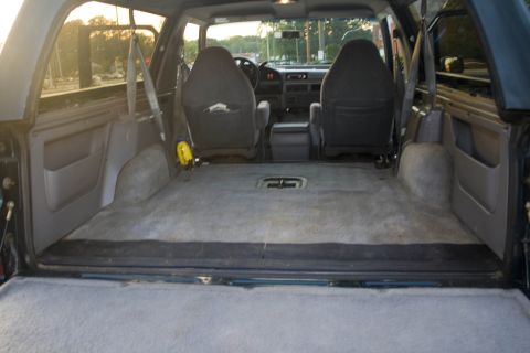 1995 Ford Bronco - View into the rear cargo area of a Ford Bronco through the open tailgate, with the rear bench seat removed to leave a flat gray carpeted fl…