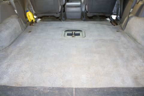 1995 Ford Bronco - Close-up of the empty rear cargo floor of a Ford Bronco with the back seat removed, showing gray carpet, exposed seat-mount brackets along…