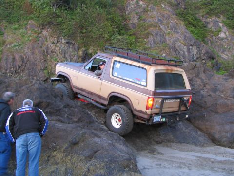 1983 Ford Bronco - A two-tone Ford Bronco navigates a rocky coastal terrain.