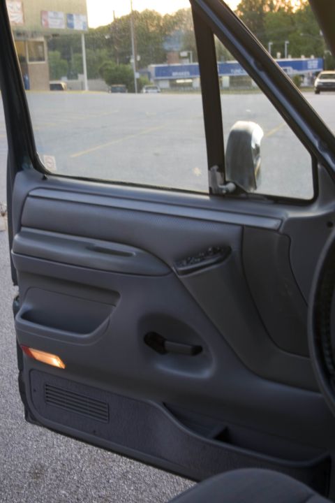 1995 Ford Bronco - Close view from inside the cab of the open passenger door on a 1990s Ford truck, showing the gray door panel with pull handle, map pocket,…
