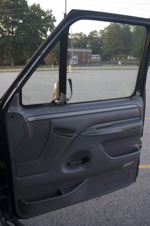 1995 Ford Bronco - Open driver's door of a dark green 1990s Ford truck showing the gray door panel with manual window crank, map pocket, door-mounted speaker…
