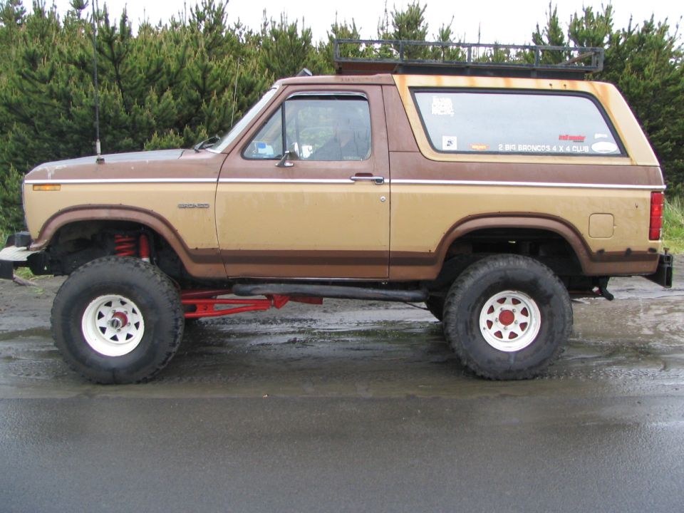 Brown and tan lifted Ford Bronco SUV in side view on white wheels with large tires