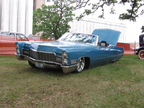 1989 Ford Mustang - A blue 1969 Cadillac convertible with its hood open and a lowered stance is parked on grass.