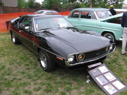 1989 Ford Mustang - A black AMC Javelin is displayed on a grassy area next to a teal-colored sedan with its hood open.