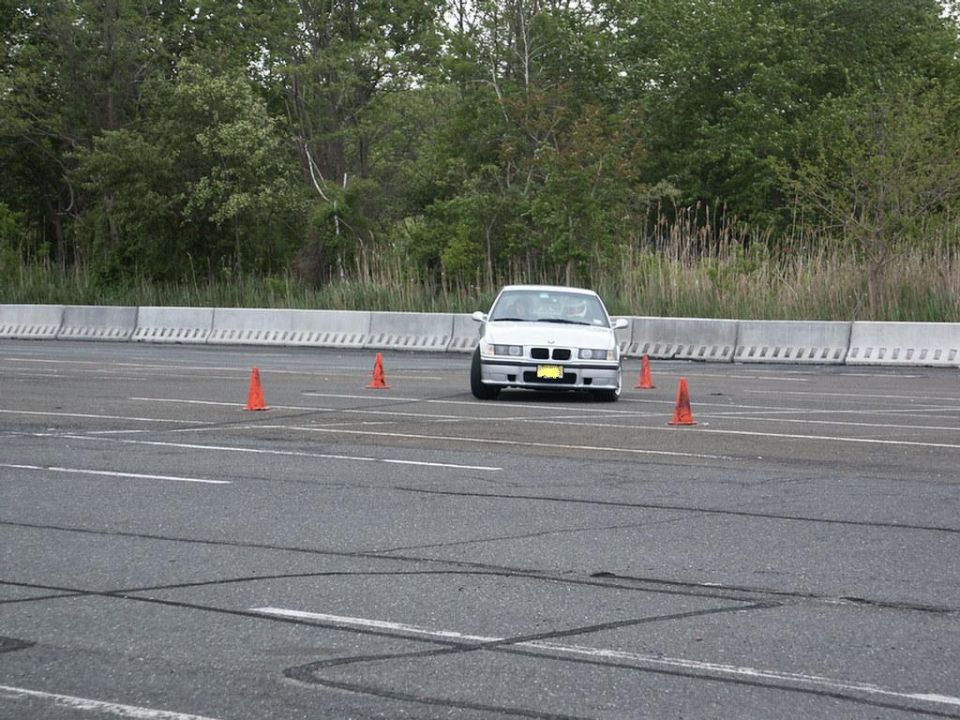 White BMW E36 driving around orange cones on a paved course