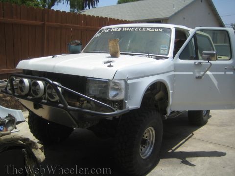1990 Ford Bronco - white lifted Ford Bronco project rig with tube bumper and light pods sits in a backyard driveway.