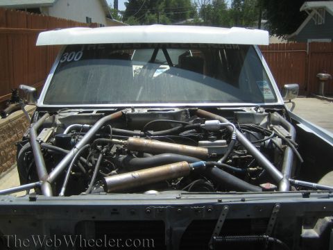1990 Ford Bronco - Front view into the engine bay of a tube-chassis race truck showing roll cage tubes, mufflers and wiring.