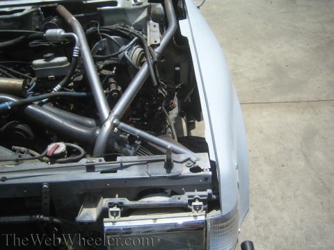 1990 Ford Bronco - tubular chassis engine bay with crossing steel tubes, radiator support and headlight, viewed in a driveway.