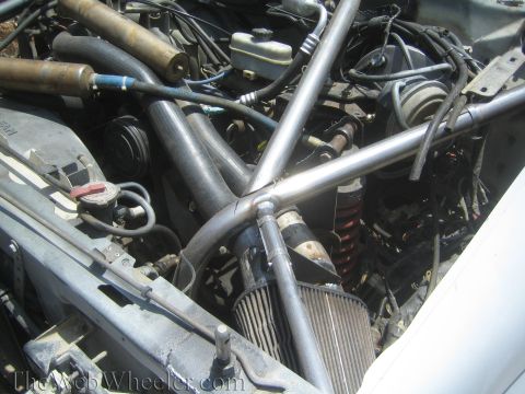 1990 Ford Bronco - Detailed view of a tubular chassis engine bay packed with hoses, wiring, a cone filter and a coil-over shock.