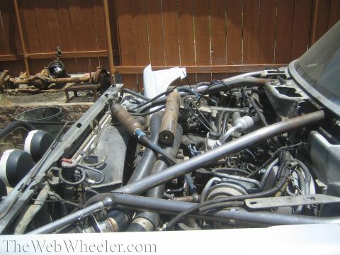 1990 Ford Bronco - open tubular chassis engine bay full of hoses and tubes, with a bare axle resting on the ground behind it.