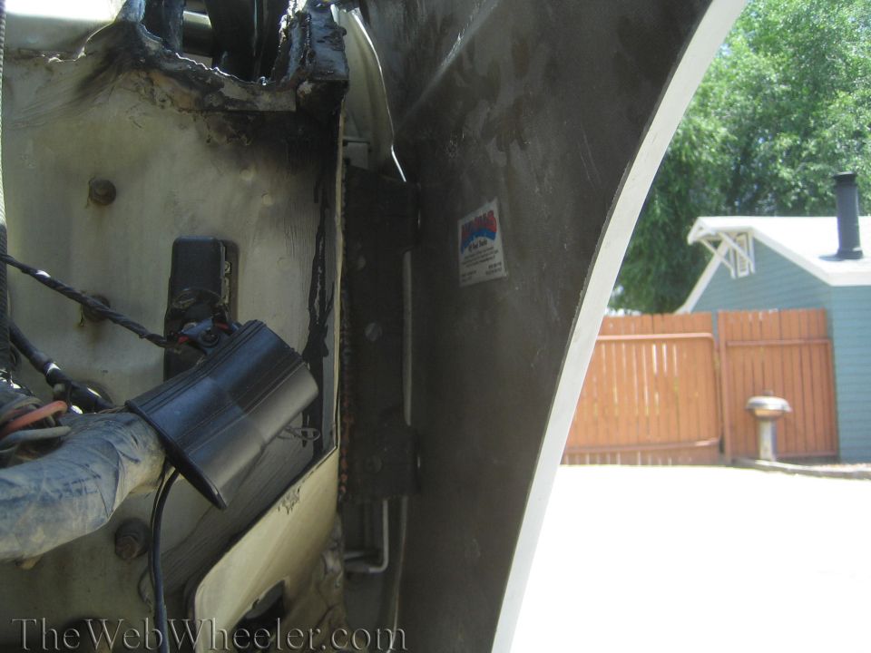 Vehicle fender well interior with wiring and a backyard fence visible